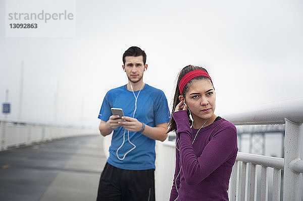 Selbstbewusste Sportlerin trägt Kopfhörer  während sie mit einem Freund auf der Bay Bridge steht