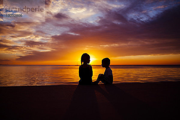 Scherenschnittgeschwister sitzen bei Sonnenuntergang am Strand