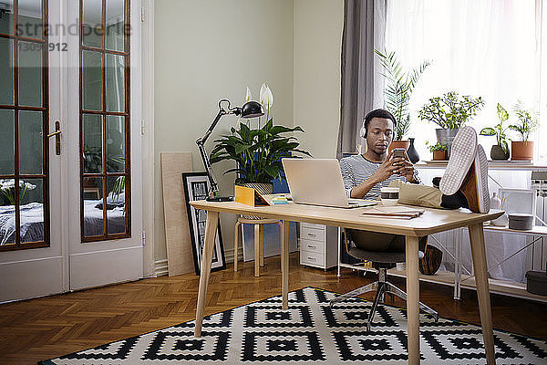 Entspannter Mann benutzt Smartphone im Heimbüro