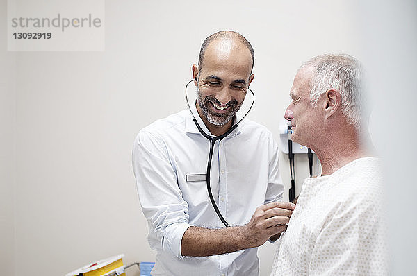 Lächelnder Arzt prüft Herzschlag des Patienten