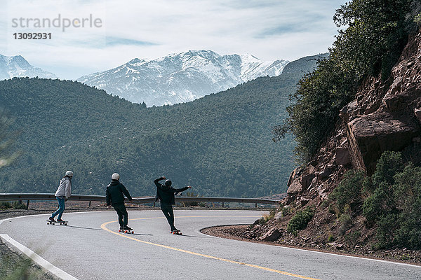 Rückansicht von Freunden beim Skateboarden auf Straße gegen Berg