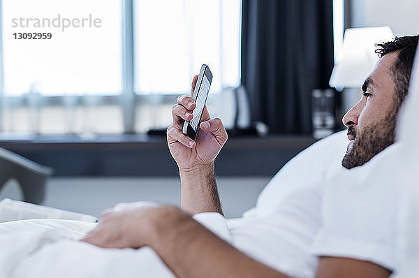 Seitenansicht eines Mannes mit einem Smartphone im Hotelzimmer
