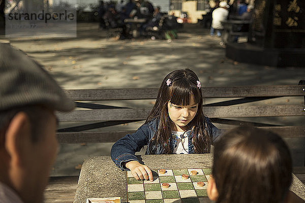 Mädchen schaut beim Damespiel mit Schwester im Park nach unten