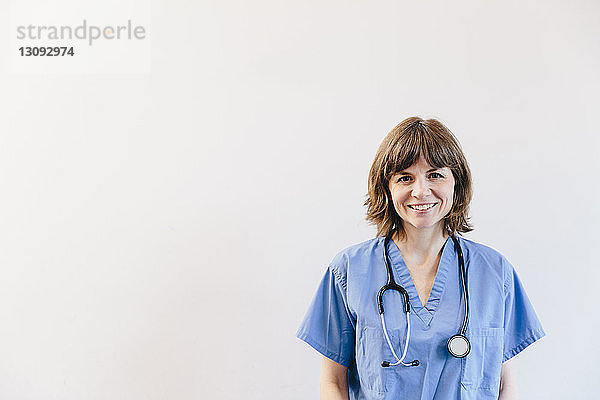 Porträt einer lächelnden Ärztin mit Stethoskop vor weissem Hintergrund stehend