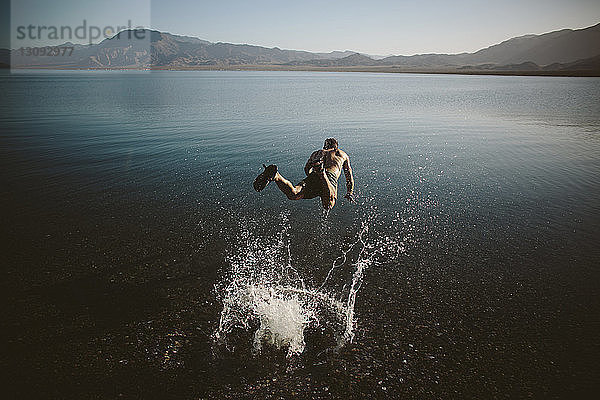 Hochwinkelaufnahme eines hemdlosen Mannes  der gegen Berge in den See springt