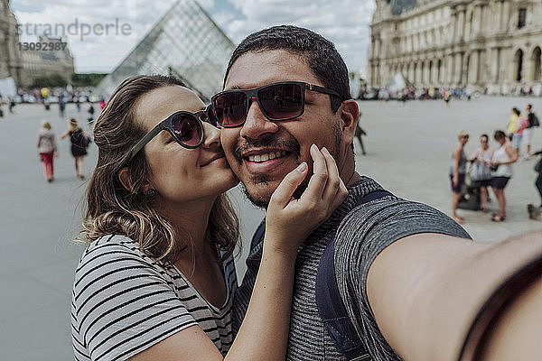 Porträt einer Freundin  die ihren Freund gegen das Musee du Louvre in der Stadt küsst