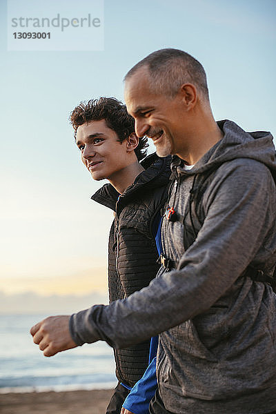 Seitenansicht eines glücklichen Vaters und Sohnes  die am Strand gegen den Himmel laufen