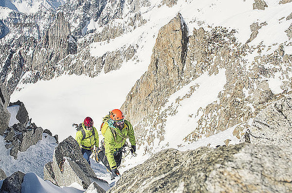 Hochwinkelaufnahme von männlichen Wanderern  die im Winter an einem sonnigen Tag den Berg besteigen