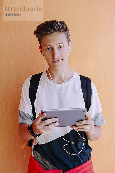 Porträt eines Mannes  der einen Tablet-Computer benutzt  während er an einer orangefarbenen Wand in der Bibliothek steht