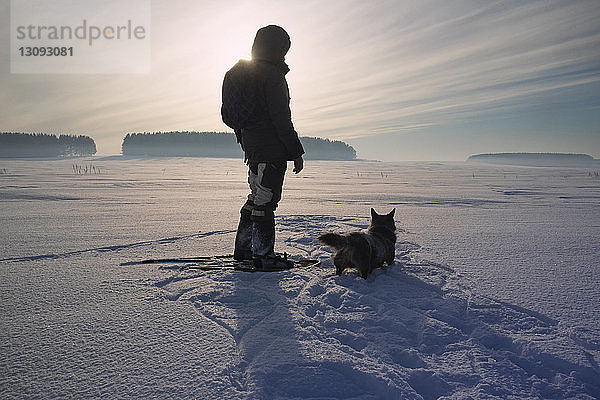 Rückansicht eines Mannes mit Hund auf schneebedecktem Feld gegen den Himmel stehend