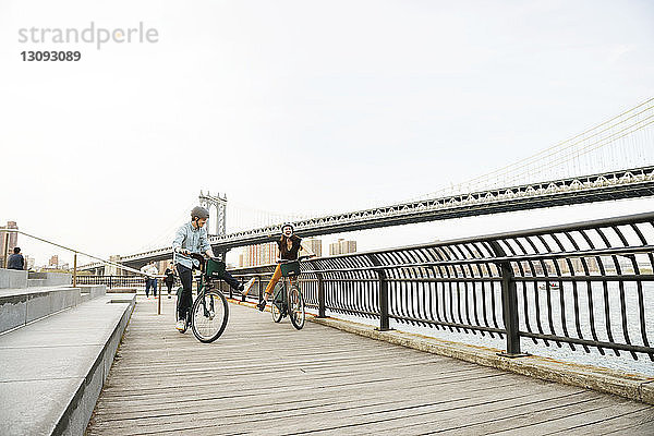 Paar genießt beim Radfahren auf dem Fußweg an der Manhattan-Brücke gegen den Himmel