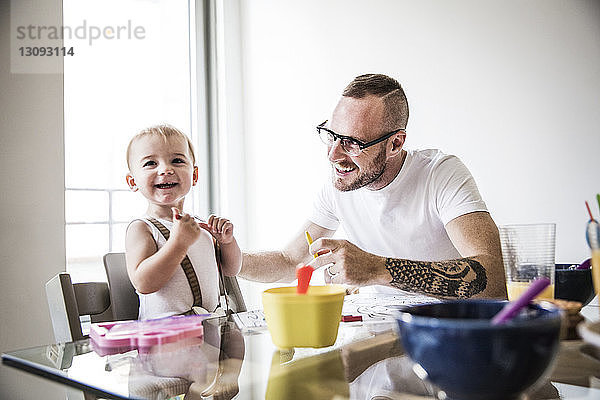 Glücklicher Vater füttert Tochter am Frühstückstisch an der Wand
