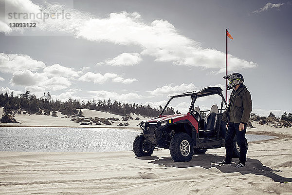 Mann mit Golfwagen auf Sand am Teich stehend