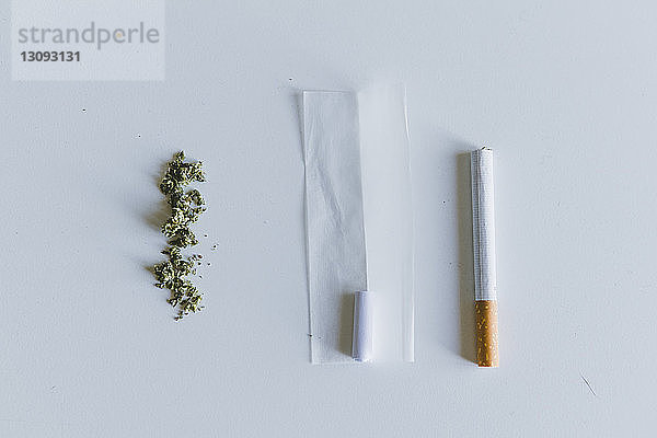 Draufsicht auf Marihuana-Joints und Zigarette mit Papier auf weißem Tisch