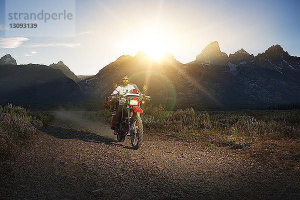 Motorrad fahrender Mann auf unbefestigter Straße gegen Berge