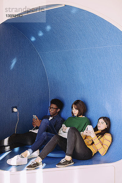 Freunde benutzen Smartphones  während sie in der Bibliothek sitzen