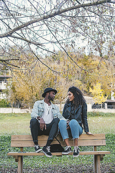Romantisches Paar schaut sich an  während es im Park auf einer Bank gegen den Himmel sitzt