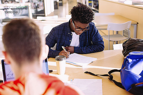 Schrägansicht von männlichen Freunden beim Lernen am Tisch in der Bibliothek