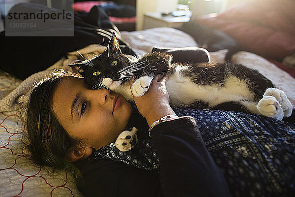Mädchen mit Katze entspannt sich zu Hause auf dem Bett