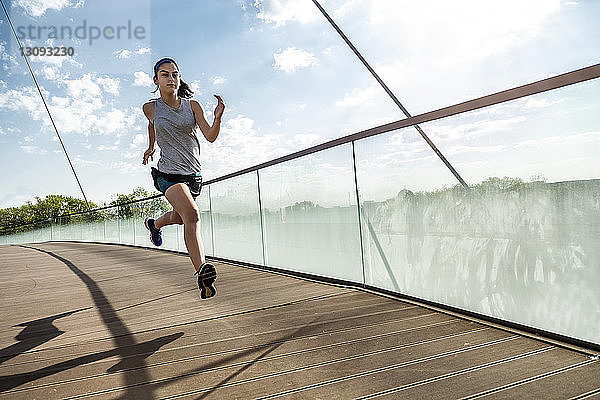 Weibliche Athletin läuft auf Brücke gegen Himmel
