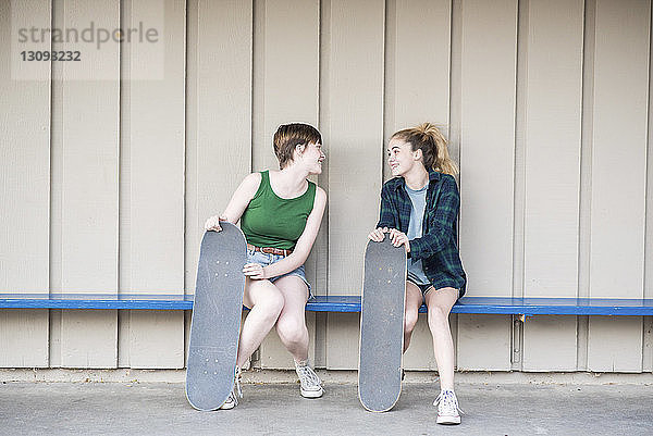 Teenager-Freunde mit Skateboards unterhalten sich  während sie auf einer Bank an der Wand sitzen
