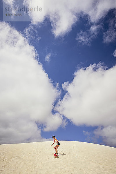 Mädchen beim Sandboarding in der Wüste vor bewölktem Himmel