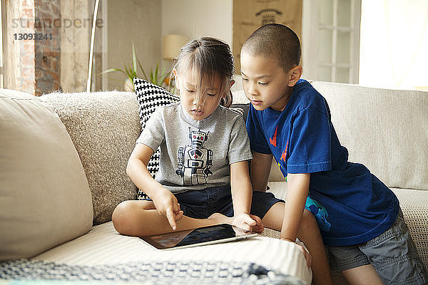 Geschwister benutzen Tablet-Computer  während sie auf dem Sofa im Wohnzimmer sitzen