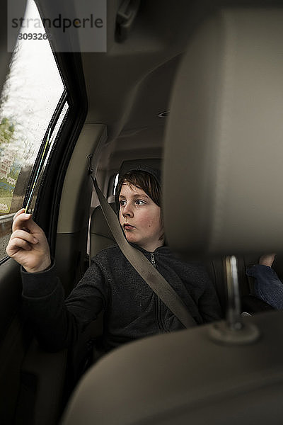 Ernsthafter Junge betrachtet Comic-Buch am Fenster  während er im Auto unterwegs ist