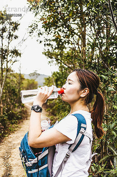 Seitenansicht einer Wanderin  die Wasser trinkt  während sie bei Pflanzen gegen den Himmel steht