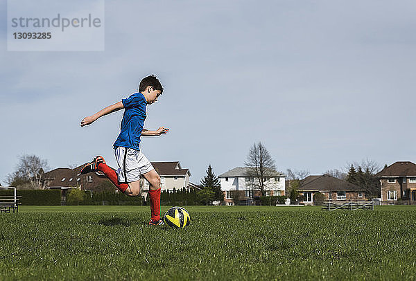 Seitenansicht eines Jungen  der beim Spielen auf einem Rasenplatz einen Fussball kickt