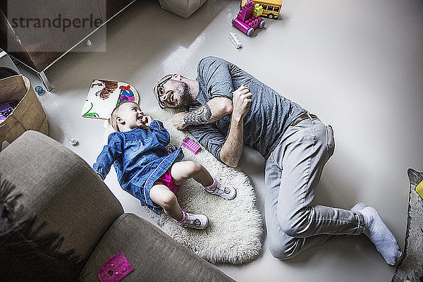 Hochwinkelaufnahme eines glücklichen Vaters und einer glücklichen Tochter  die zu Hause auf dem Boden liegen