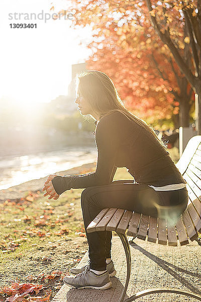 Seitenansicht einer jungen Frau  die auf einer Parkbank sitzt