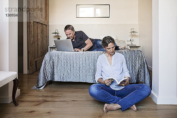 Älteres Ehepaar mit Laptop und Lesebuch im Schlafzimmer