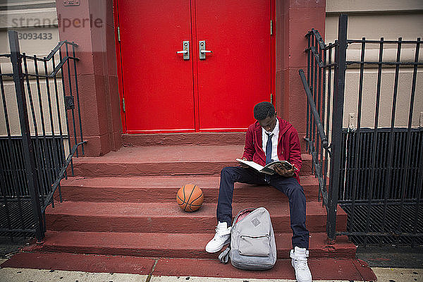 Schüler lesen Buch  während sie beim Basketball auf Stufen vor dem Haus sitzen