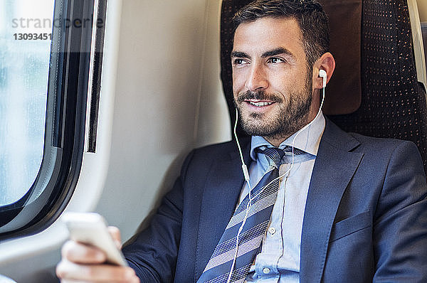 Lächelnder Geschäftsmann hört im Zug Musik über Smartphone