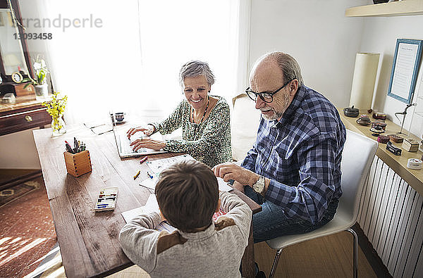 Glückliche Großeltern helfen dem Jungen zu Hause beim Zeichnen