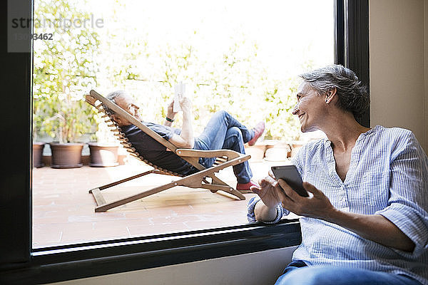 Glückliche Frau sieht älteren Mann an  der auf einem Liegestuhl auf der Veranda sitzt