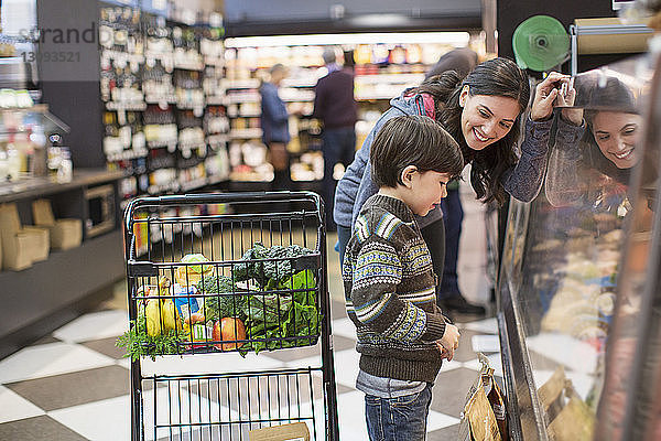 Lächelnde Frau sieht Sohn an  der an einer Vitrine im Supermarkt steht