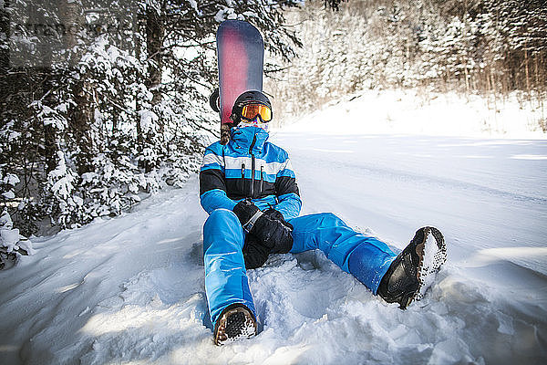 Mann mit Snowboard entspannt sich auf schneebedecktem Feld