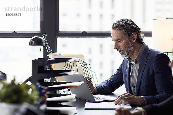 Geschäftsmann arbeitet an Laptop-Computer gegen Fenster im Büro