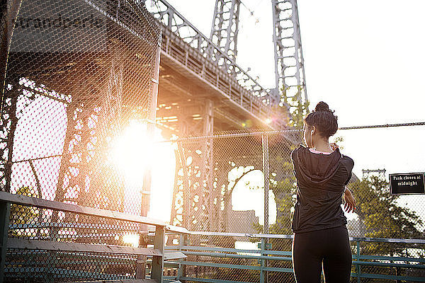 Rückansicht einer Frau  die sich an einem sonnigen Tag gegen die Williamsburg Bridge streckt