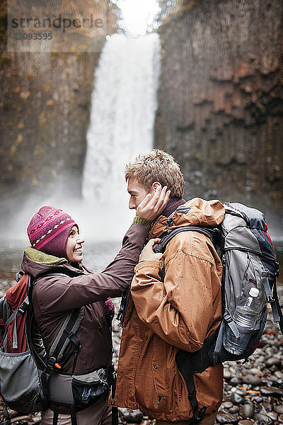 Glückliche Wanderin berührt das Gesicht eines Mannes  während sie am Wasserfall steht