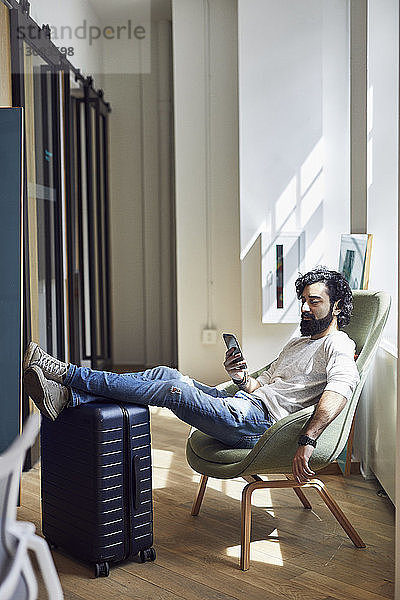 Geschäftsmann benutzt Smartphone  während er im Kreativbüro auf einem Stuhl sitzt