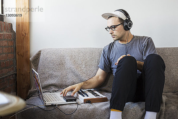 Mann hört Musik  während er einen Laptop-Computer auf dem Sofa benutzt