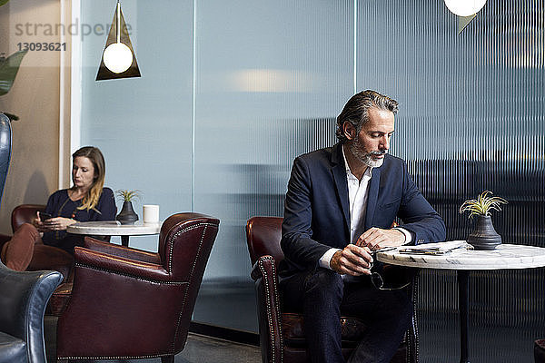Geschäftsmann liest Buch  während eine Geschäftsfrau ein Smartphone in der Cafeteria des Kreativbüros benutzt