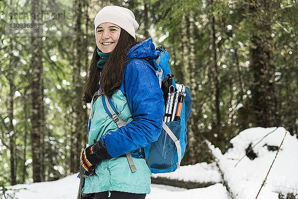Porträt einer lächelnden Frau mit Rucksack  die im Winter im Wald steht