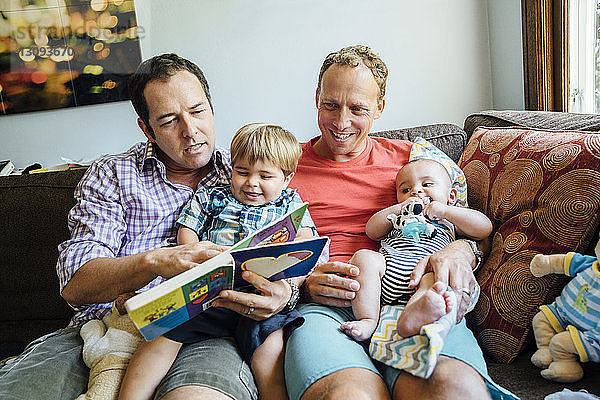 Homosexuelles Paar liest Buch mit Söhnen auf dem Sofa zu Hause