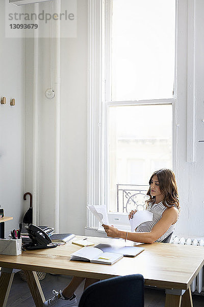 Geschäftsfrau prüft Dokumente  während sie im Büro am Schreibtisch sitzt