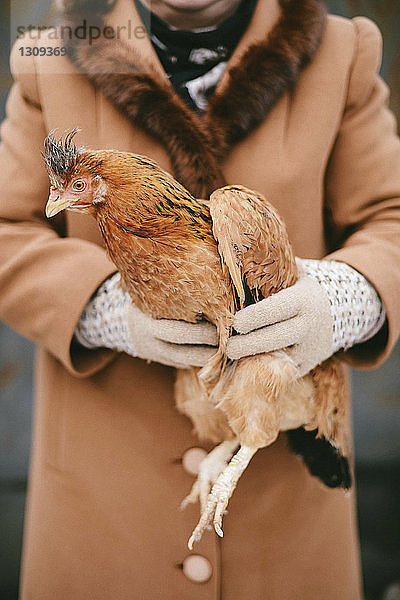 Mitte einer Frau  die Hühner hält  während sie im Freien steht