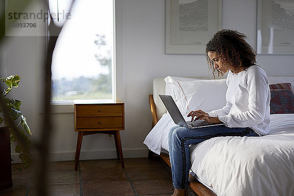 Frau benutzt Laptop-Computer  während sie zu Hause im Bett sitzt